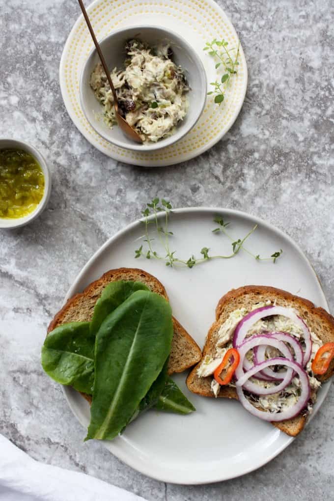 Bread with lettuce, onions and fish layered on it to make sandwich.