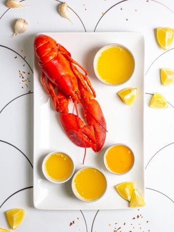 lobster on a platter with butter sauce, lemon wedges + garlic