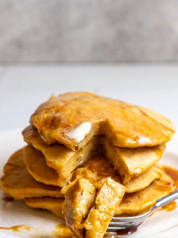 pancakes stacked on a plate, topped with butter and syrup.