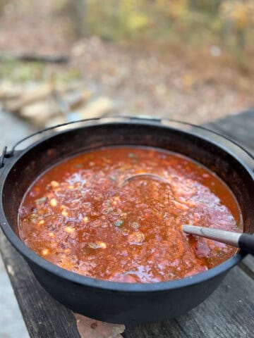 Campfire chili in Dutch oven sitting on picnic table.