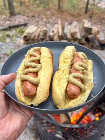 Two campfire hot dogs and sauerkraut inside brioche buns topped with swirls of mustard.