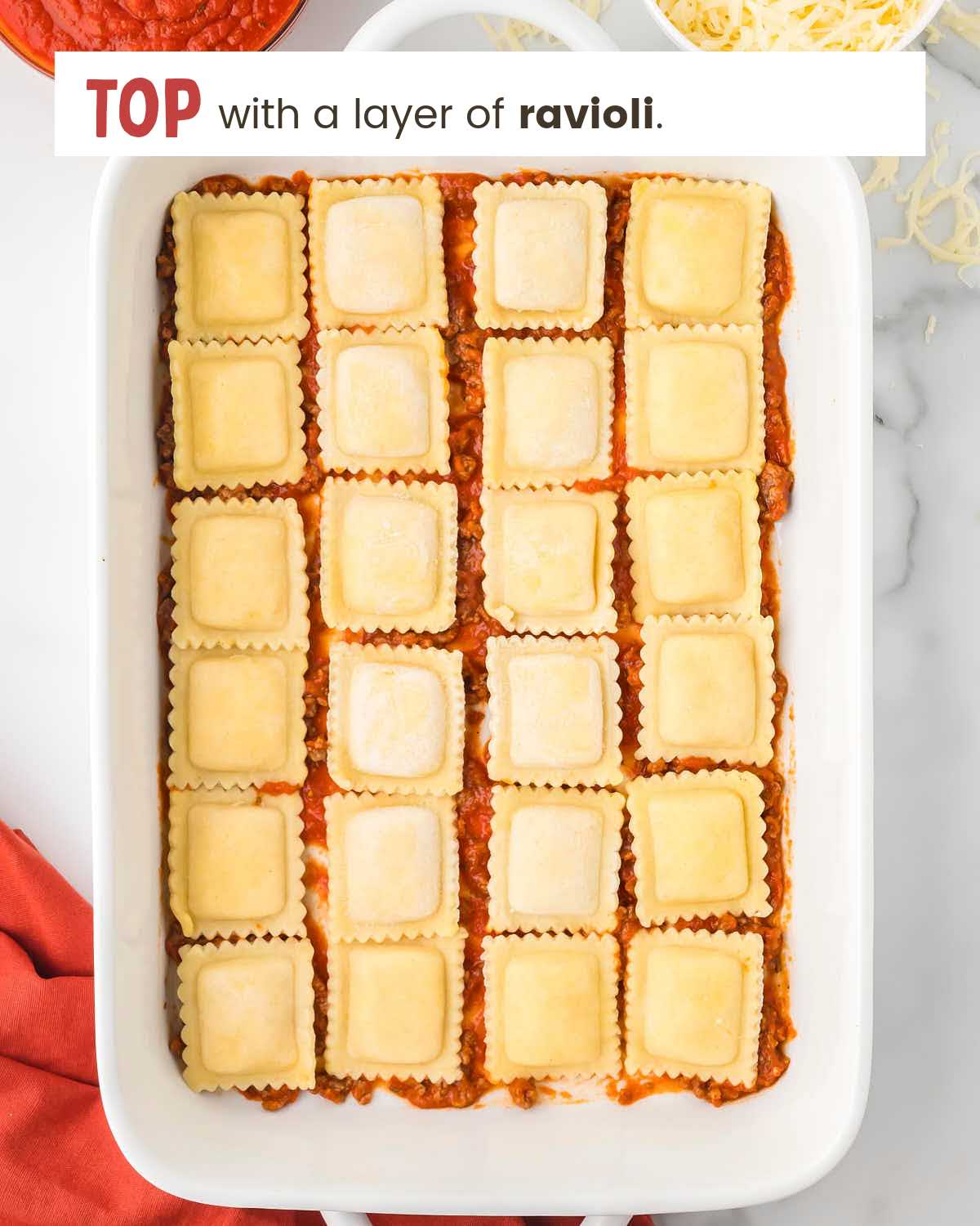 A layer of ravioli squares over meat sauce in a baking dish.