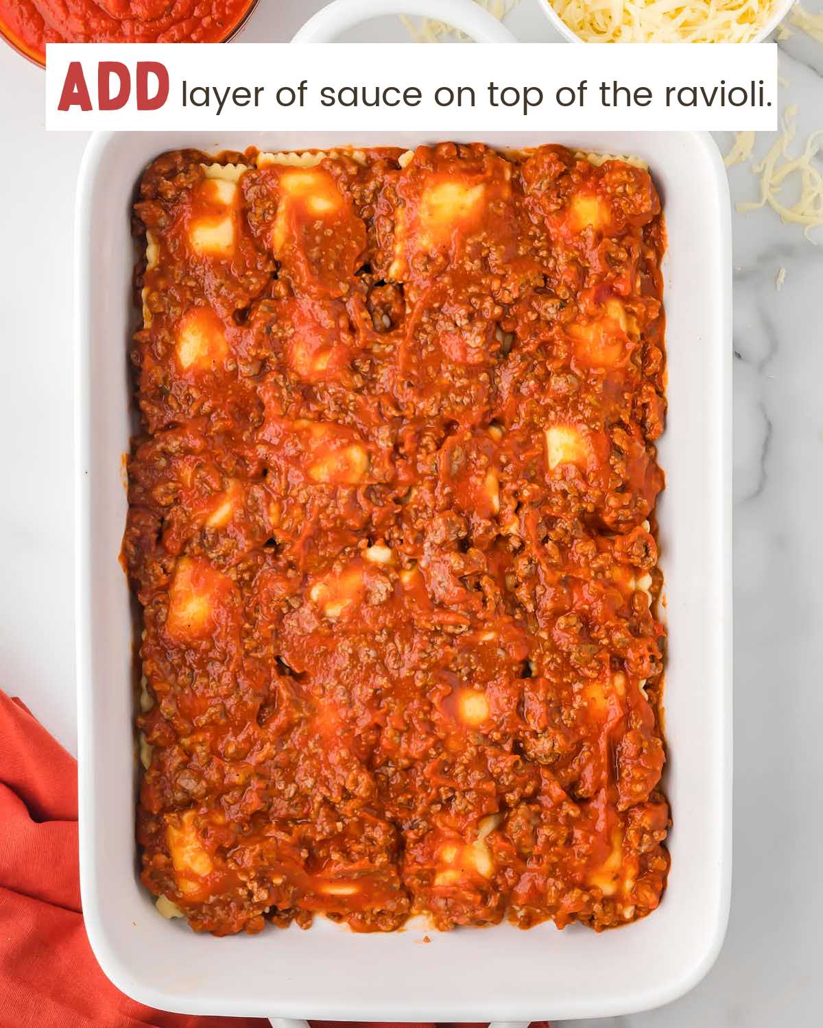 A layer of meat sauce over ravioli squares in a baking dish.