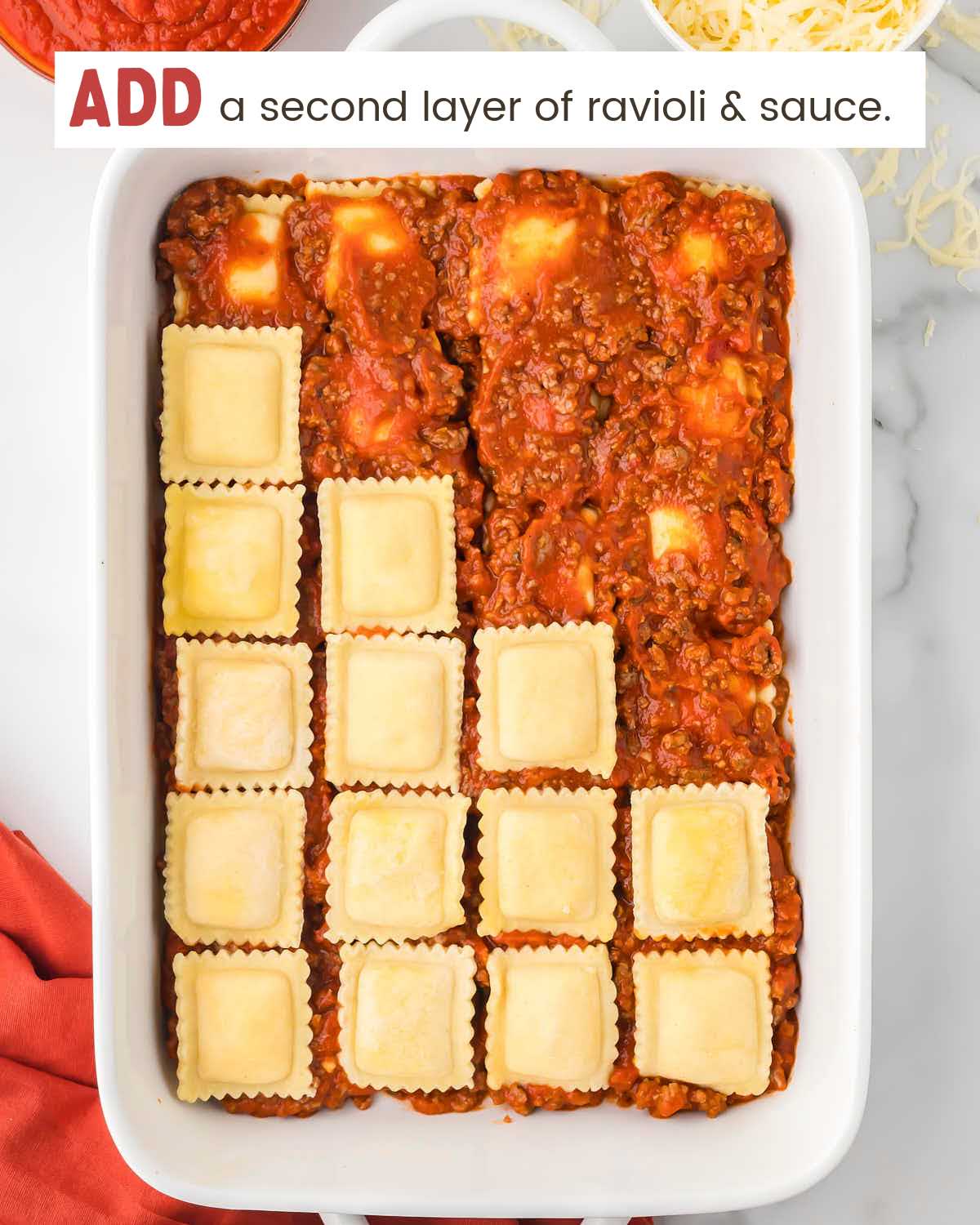 A partial layer of ravioli squares over meat sauce in a baking dish.