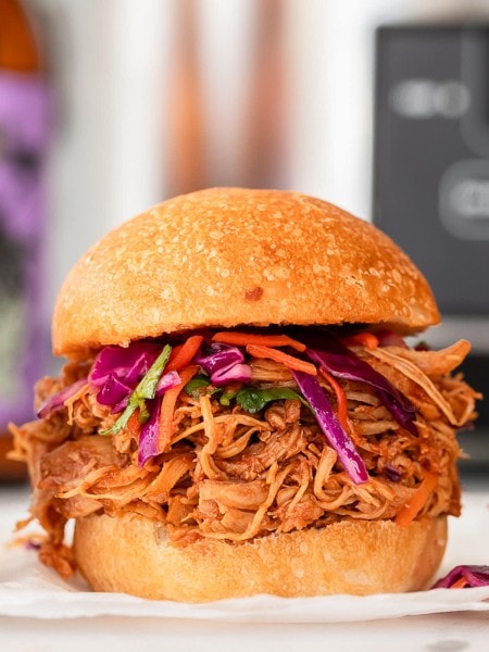 A slow cooker pulled chicken slider with slaw on a white plate.