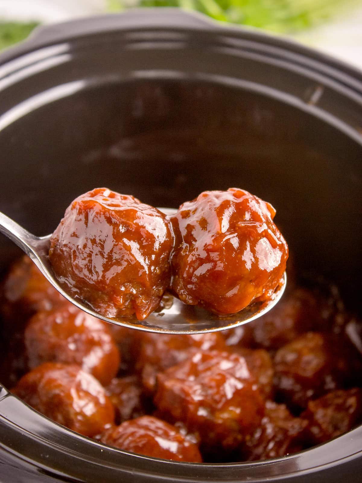 A large serving spoon removing barbecued meatballs from a Crcokpot.