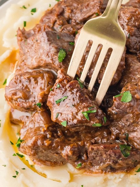 Closeup of a fork stuck into a piece of Steak Bites cooked in an Crockpot.