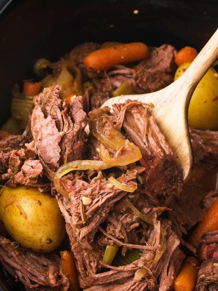 A wooden spoon removing cooked Slow Cooker Sirloin Tip Roast.