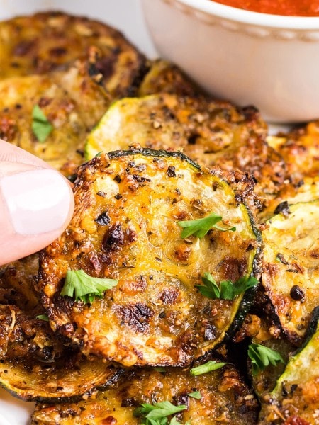 Holding up a slice of air-fried Zucchini Chips.