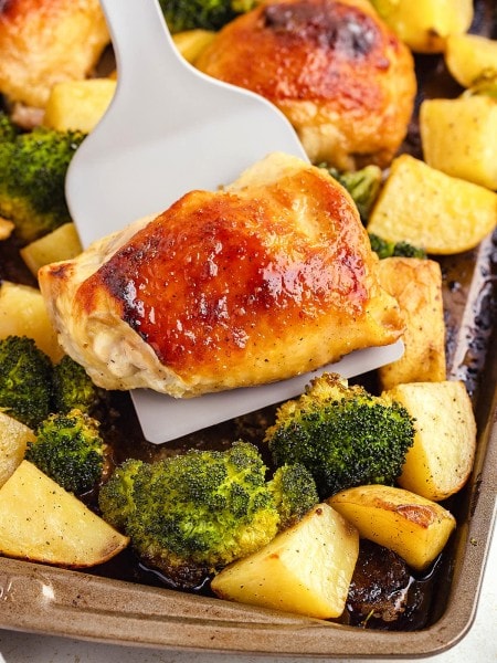 Lifting chicken thighs off a sheet pan.