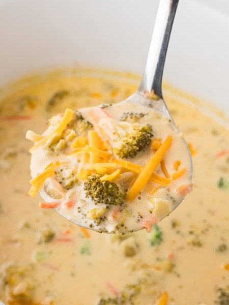 A ladle of Cheddar Broccoli Soup in a white Crockpot.