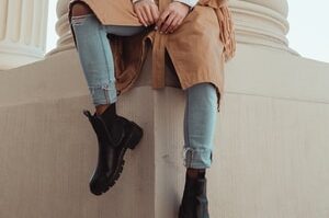 woman in brown leather jacket and blue denim jeans holding black leather bag