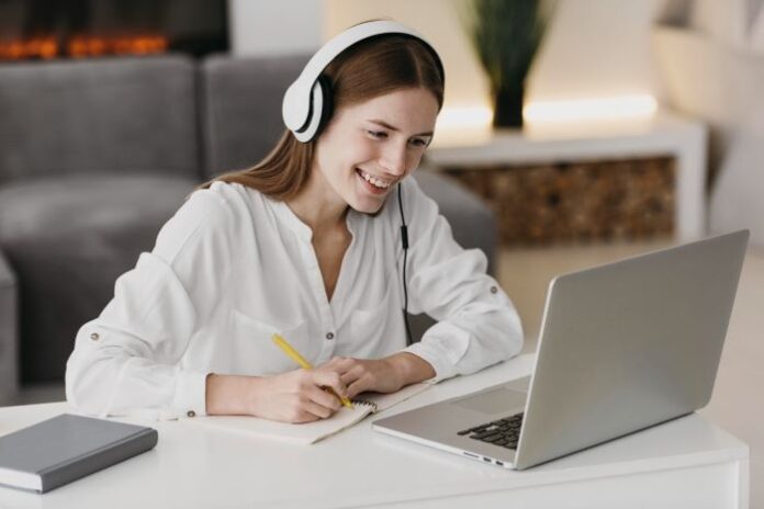 Adult student learning through online education, sitting in front of a laptop and taking notes