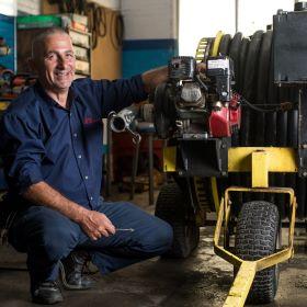 A man kneeling next to a hose in a garage.