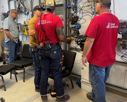 A group of men in C&W Services shirt being shown how to use maintenance equipment