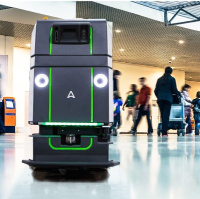 A robot walking through an airport with people around it.