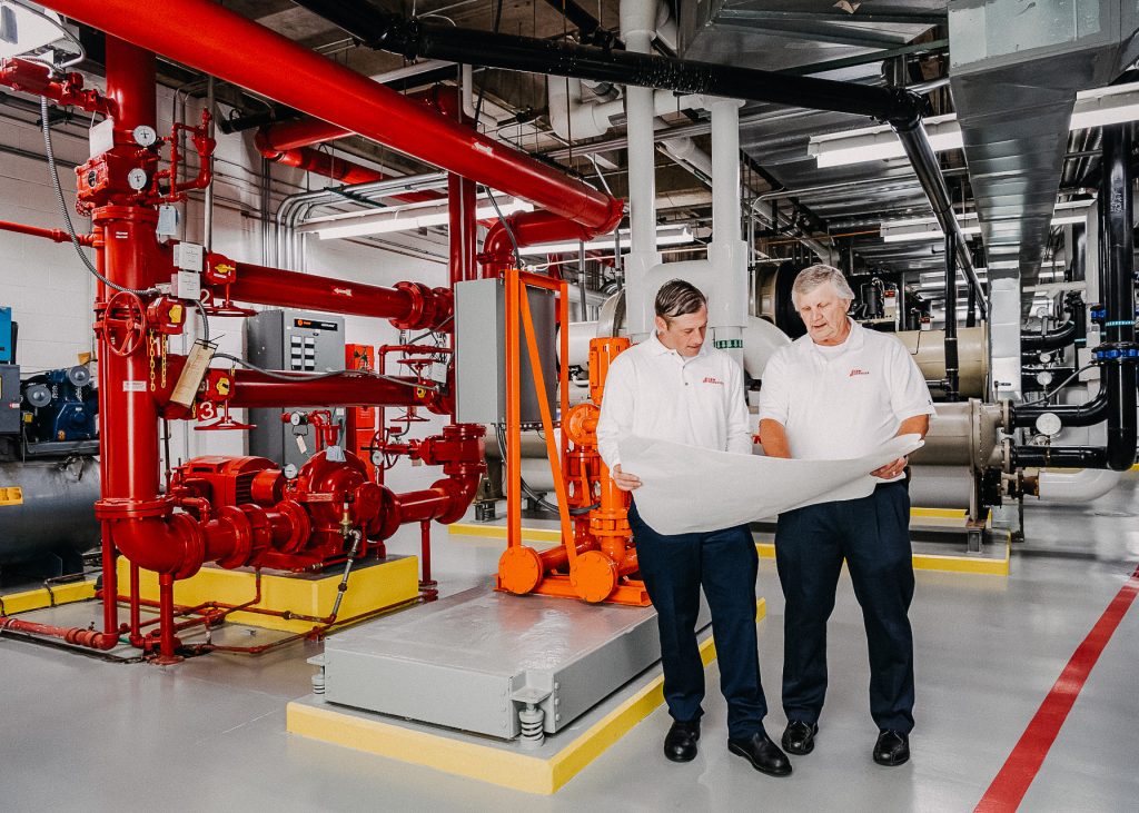 Two men standing in a HVAC area looking at a plan.