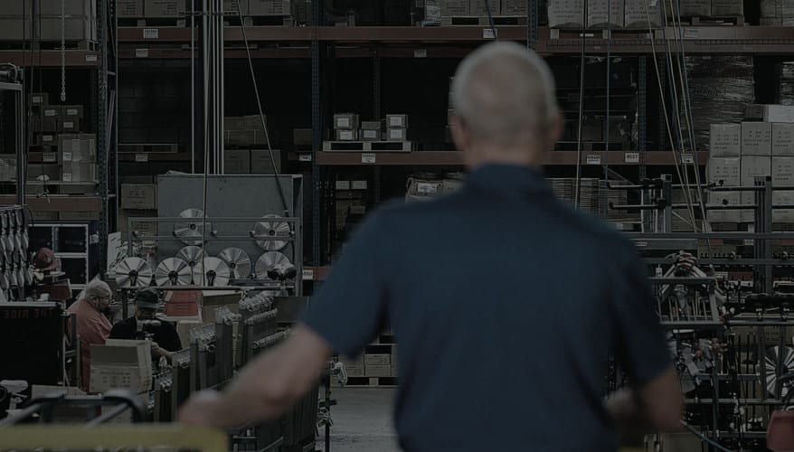 Dennis Keiser facing away from camera looking out over Keiser factory floor with workers manning assembly line stations