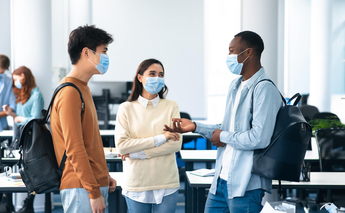 Friends at high school wearing mask and talking: Healthcare, Education, Lifestyle And People Concept. Group of smiling diverse international students wearing protective medical masks and talking, standing in lecture hall at the university