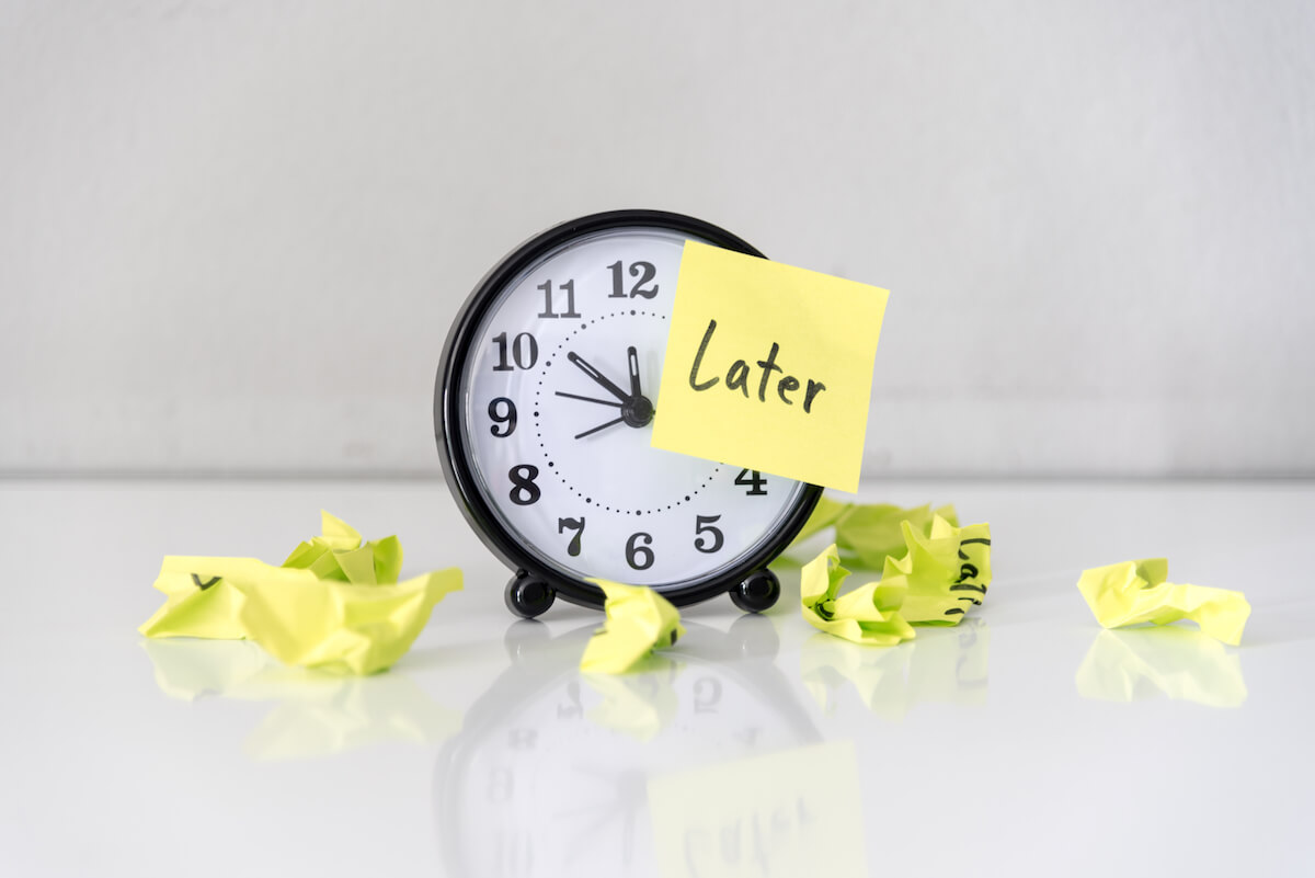 Clock with post it notes saying "later": Shutterstock: Procrastination delay and urgency concept with word later on sticky paper over white alarm clock and crumpled paper ball, bad time management.