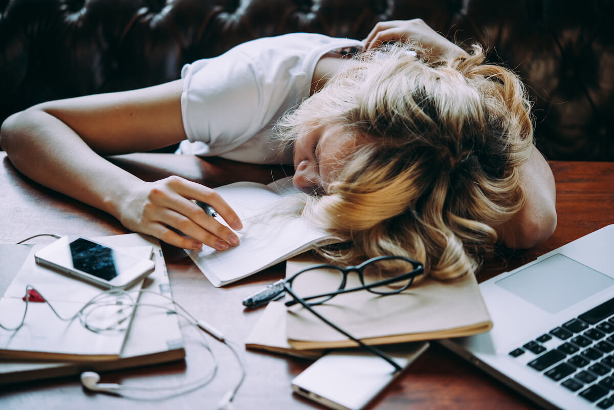 Woman bored and procrastinating her work: Shutterstock: A tired teenage girl sleeping on her table while doing her school homework. Laziness and procrastination concept