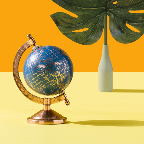 An antique globe resting on a yellow surface and vase with a large, tropical leaf.