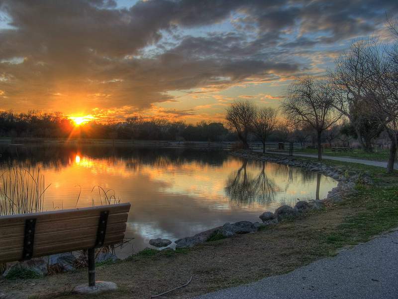 Sonnenuntergang am Ufer des Hellyer County Park mit einer Bank und einem Wanderweg im Vordergrund.