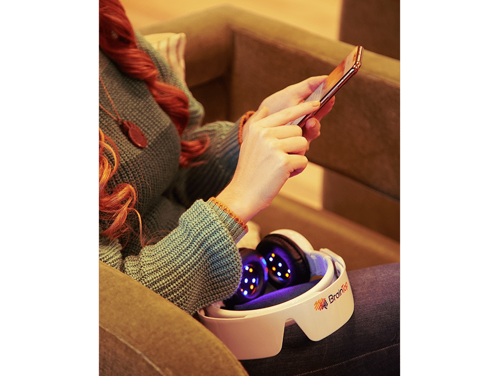 Person holding the BrainTap device on their lap while looking at the app on a smartphone