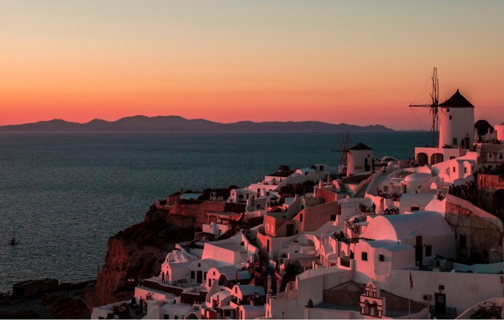 Sunset in Santorini: white buildings on the right bask in beautiful evening light, looking over the sea with land beyond