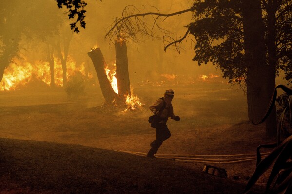 A firefighter runs while battling the Thompson Fire burning in Oroville, Calif., Tuesday, July 2, 2024. An extended heat wave blanketing Northern California has resulted in red flag fire warnings and power shutoffs. (AP Photo/Noah Berger)
