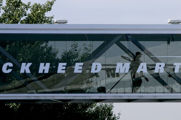 FILE - A man walks past a Lockheed Martin logo as he walks through a section of the company's chalet bridging a road at Farnborough International Airshow in Farnborough, southern England, July 19, 2006. China says it has banned a number of business units of American aviation maker Lockheed Martin and three of its executives over arms deals with Taiwan, the self-ruling island it claims as its own territory. (AP Photo/Matt Dunham, File)