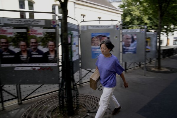 A woman walks past campaign boards for the upcoming parliamentary elections in Paris, Thursday June 27, 2024. Voters will choose lawmakers for the National Assembly in two rounds on June 30 and July 7. (AP Photo/Christophe Ena)