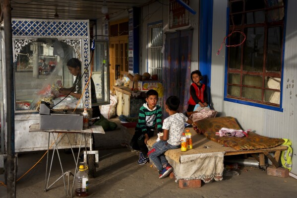 FILE - A Uyghur woman works at her food stand while her children play in a resting place nearby at the Unity New Village in Hotan, in western China's Xinjiang region on Sept 20, 2018. Authorities in China's western Xinjiang region have been systematically replacing the names of villages inhabited by Uyghurs and other ethnic minorities to reflect the ruling Communist Party's ideology, as part of an attack on their cultural identity, according to a report released Wednesday, June 19, 2024 by Human Rights Watch. (AP Photo/Andy Wong, File)