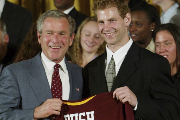 FILE - President Bush, left, holds up a jersey presented to him by Grant Potulny, right, captain of the University of Minnesota men's ice hockey, as the 2003 NCAA champions were honored in the East Room of the White House in Washington, June 17, 2003. Potulny is leaving Northern Michigan to become the coach of the New York Rangers' American Hockey League affiliate in Hartford, Connecticut. Rangers president and general manager Chris Drury announced the hiring of the 44-year-old Potulny on Thursday, June 27, 2024.(AP Photo/Pablo Martinez Monsivais, File)