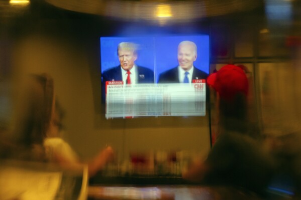 Seen through a beer glass, patrons look on during a watch party of the presidential debate between President Joe Biden and Republican presidential candidate former President Donald Trump at Old Louisville Tavern on Thursday, June 27, 2024, in Louisville, Ky. (AP Photo/Jon Cherry)