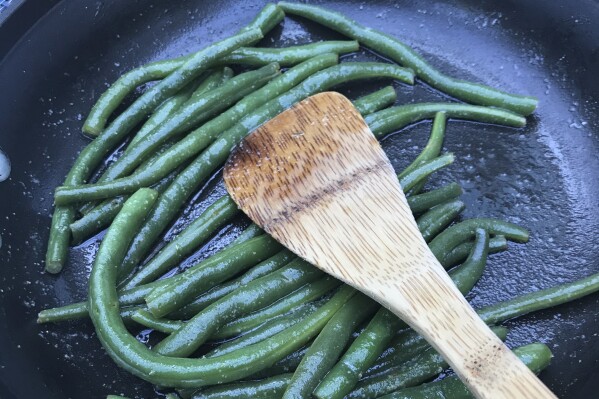 A plate of green beans picked from a home garden is prepared in a saute pan in Chatham, Mass. on July 28, 2021. Nutrition experts say you can improve your health anywhere by mimicking at least one aspect of the diet — eat whatever fruits and vegetables are in season. (AP Photo/Carolyn Lessard)
