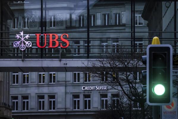 FILE - A traffic light signals green in front of the logos of the Swiss banks Credit Suisse and UBS in Zurich, Switzerland, March 19, 2023. UBS says it has completed its takeover of embattled rival Credit Suisse. The announcement comes nearly three months after the Swiss government hastily arranged a rescue deal to combine the country’s two largest banks. (Michael Buholzer/Keystone via AP, File)