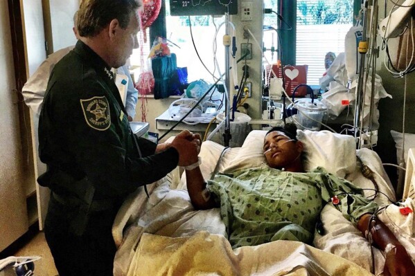 In this photo provided by the Broward County Sheriff's Office on Sunday, Feb. 18, 2018, Sheriff Scott Israel, holds the hand of Anthony Borges, 15, a student at Marjory Stoneman Douglas High School. Borges, the most severely wounded survivor of the 2018 massacre at Parkland's Marjory Stoneman Douglas High School, now owns shooter Nikolas Cruz's name and Cruz cannot give any interviews without his permission, under a settlement reached in a lawsuit, his attorney said Thursday, June 27, 2024. (Broward County Sheriff's Office via AP)