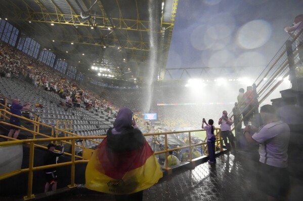 People take photos of rainwater pouring from the roof of the stadium as the match is suspended due to adverse weather during the round of sixteen match between Germany and Denmark at the Euro 2024 soccer tournament in Dortmund, Germany, Saturday, June 29, 2024. (AP Photo/Martin Meissner)
