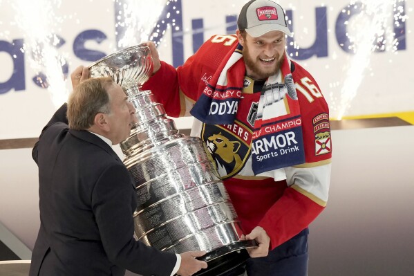 NHL Commissioner Gary Bettman, left, presents Florida Panthers forward Aleksander Barkov (16) with the NHL hockey Stanley Cup after winning the Final against the Edmonton Oilers in Sunrise, Fla., Monday, June 24, 2024. (Nathan Denette/The Canadian Press via AP)
