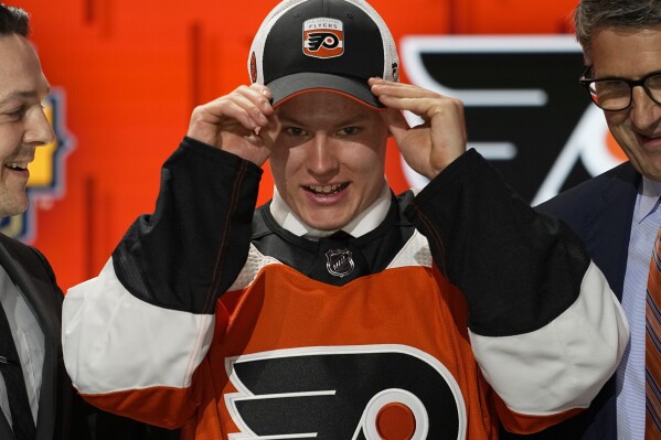 FILE - Matvei Michkov, center, adjusts his Philadelphia Flyers cap after being picked by the team during the first round of the NHL hockey draft June 28, 2023, in Nashville, Tenn. A person with knowledge of the situation tells The Associated Press that top Flyers prospect Michkov is being released by KHL club SKA Saint Petersburg. The move is the first step toward Michkov joining the Flyers ahead of the schedule. (AP Photo/George Walker IV, File)