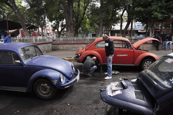 Volkswagen Beetle taxi drivers change a flat tire in the Cuautepec neighborhood of Mexico City, Friday, June 21, 2024. Mechanics in the area say driving a Volkswagen Beetle or “vocho” as it’s known in Mexico, is a dying tradition because parts have been harder to come by since Volkswagen halted production five years ago. (AP Photo/Aurea Del Rosario)