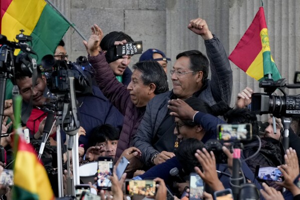 Bolivian President Luis Arce raises a clenched fist surrounded by supporters and media, outside the government palace in La Paz, Bolivia, Wednesday, June 26, 2024. Armored vehicles rammed the doors of Bolivia's government palace Wednesday in an apparent coup attempt against Arce, but he vowed to stand firm and named a new army commander who ordered troops to stand down. (AP Photo/Juan Karita)