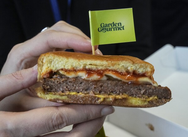 FILE - A member of the media displays a veggie cheese burger during a presentation of a veggie food line for spectators and athletes at the headquarters of the 2024 Paris Olympics in Paris on Dec. 12, 2023. (AP Photo/Michel Euler, File)