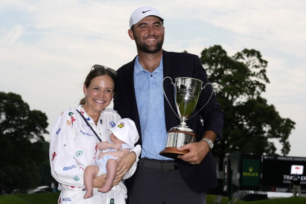 Scottie Scheffler, right, poses with his baby son Bennett and his wife Meredith after winning the Travelers Championship golf tournament at TPC River Highlands, Sunday, June 23, 2024, in Cromwell, Conn. (AP Photo/Seth Wenig)