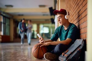 High school students with headphones using smart phone in a hallway.