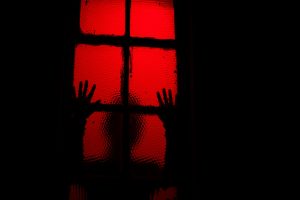 Silhouette of person leaning against window in room with red light