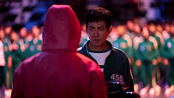 Lee Jung-jae as Seong Gi-hun looks at a man wearing a red-hooded jumpsuit in Season 2 of 'Squid Game.'