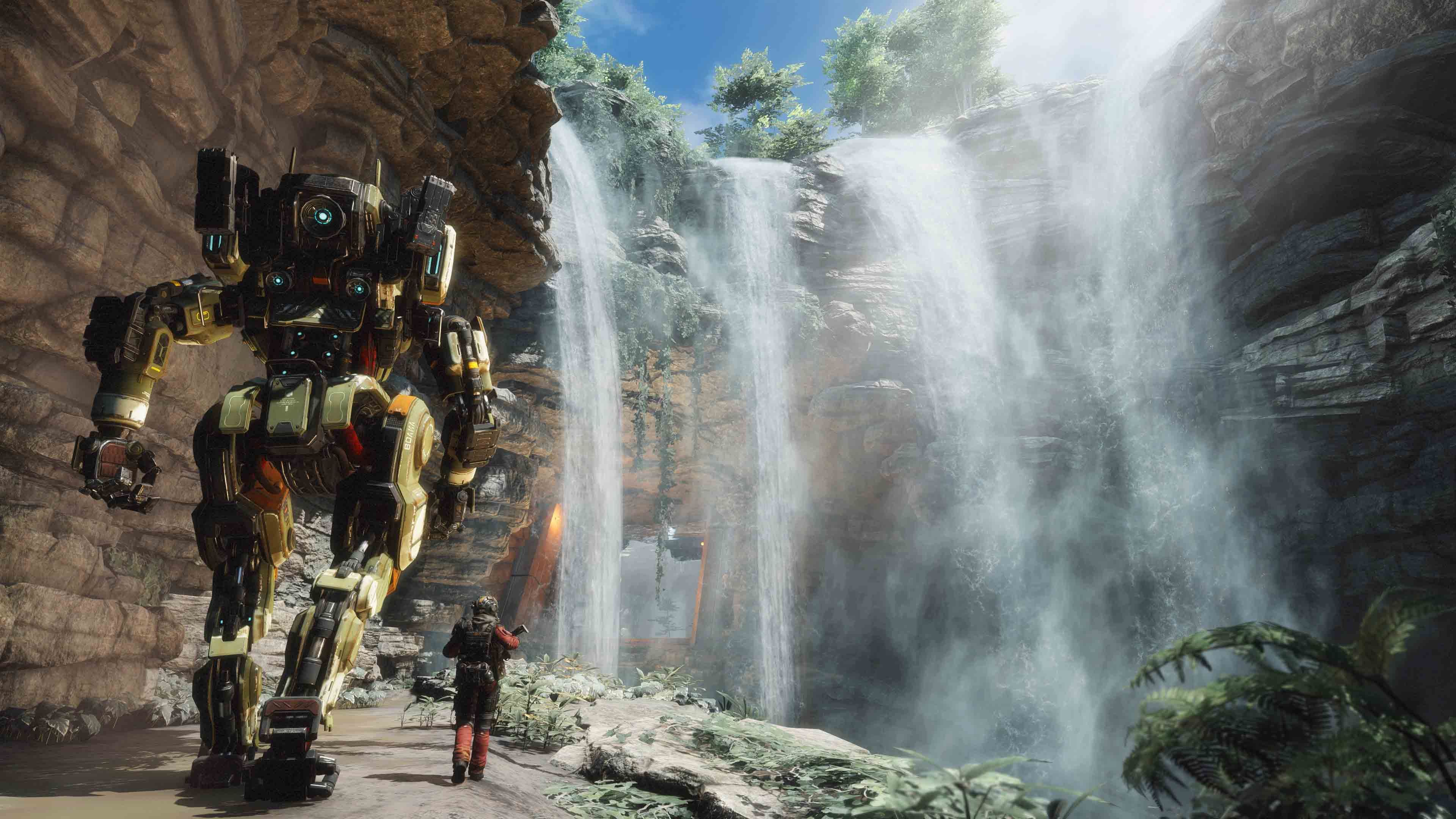 A titan and pilot walk together on a cliff towards a waterfall.