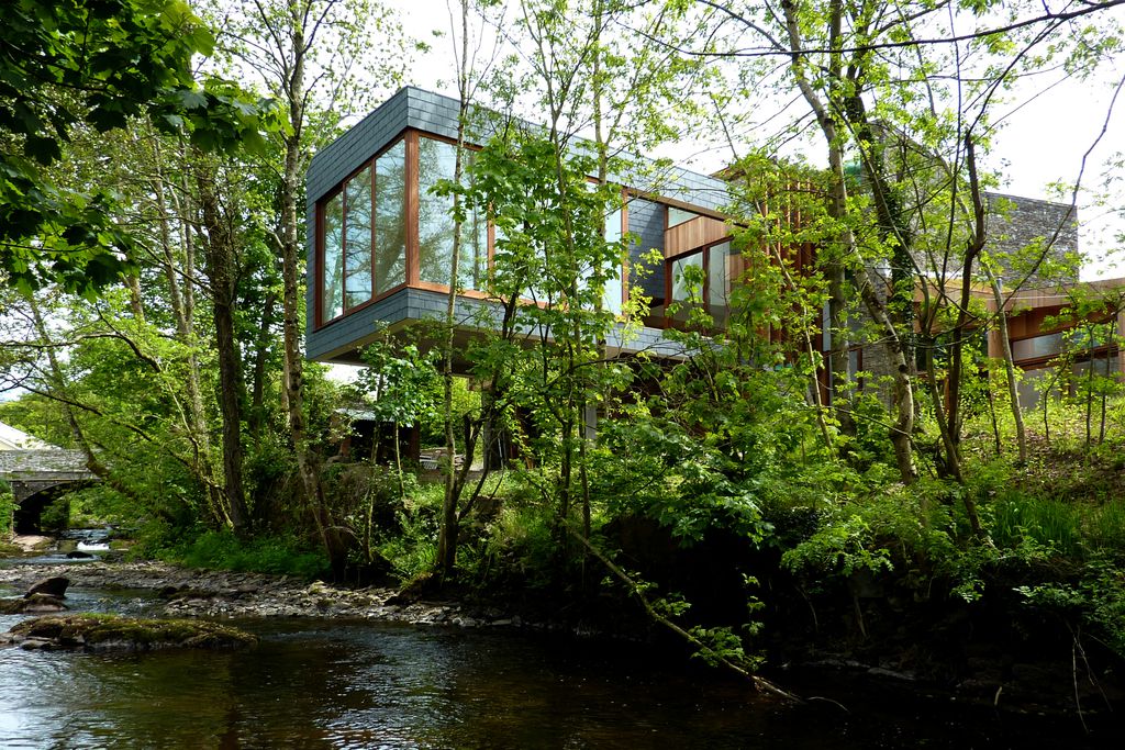 View of Ty Hedfan in Brecon, Powys, Wales through the trees - a stylish building with glass windows, right next to the river